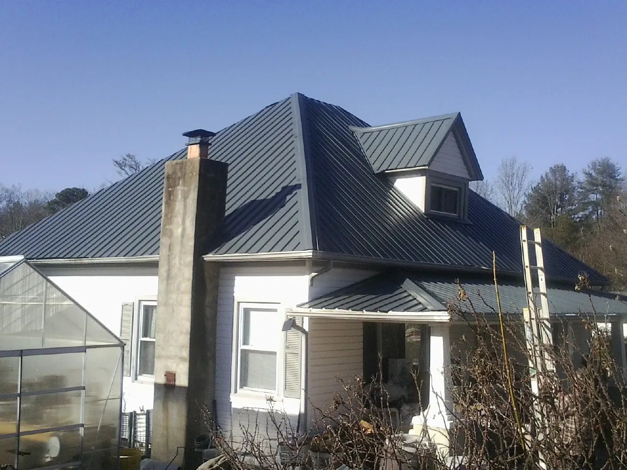 Dark blue standing seam metal roof on a white farmhouse with dormer — Slate & Tile Roof Repair by Roofing Brothers in Prosperity