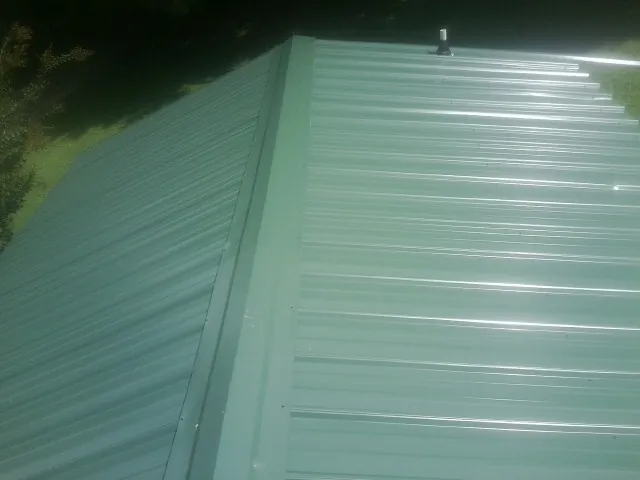 New green metal panels meeting at the ridge of a roof — Flat Roof Repair work by our crew in Prosperity