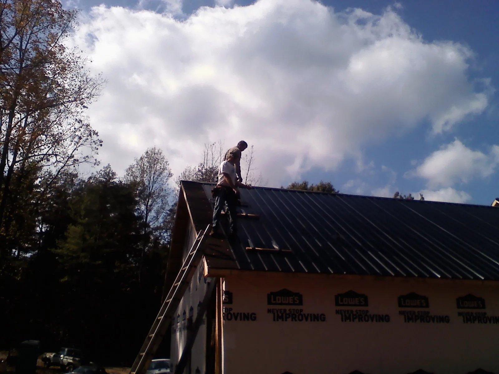 Roofer fastening dark metal panels high against a cloudy sky, from a Roof Inspection job in Prosperity