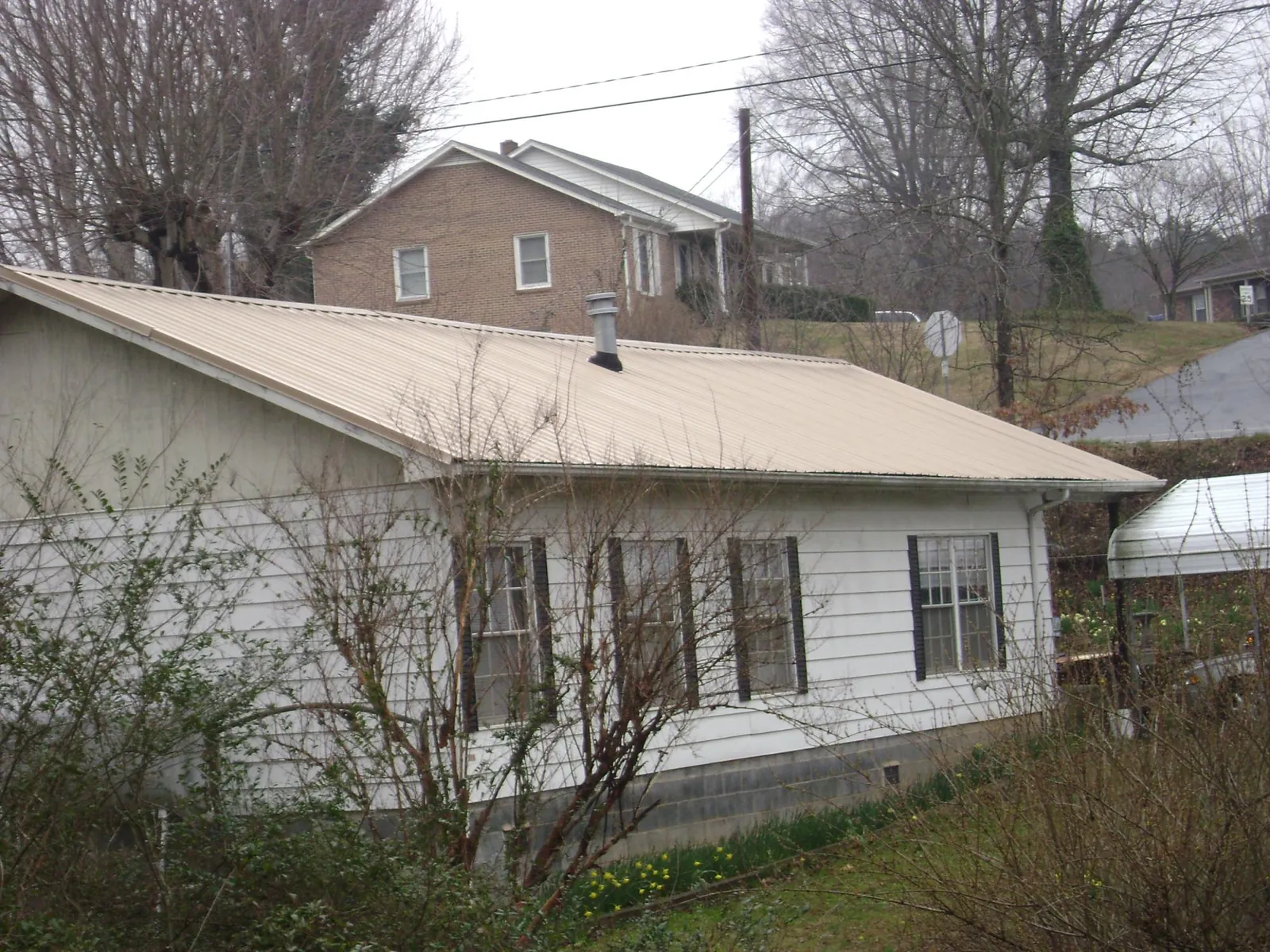 Tan metal roof on a white sided house set into a hillside — Commercial Roofing by Roofing Brothers in Prosperity